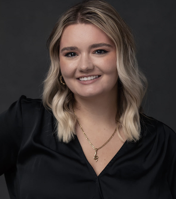 Blonde woman in black top smiling at camera, professional headshot.