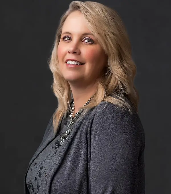 Blonde woman smiling, wearing gray cardigan for professional headshot.