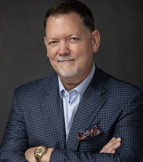 Attorney Dean Boyd smiling, arms crossed in blue blazer, against dark background.