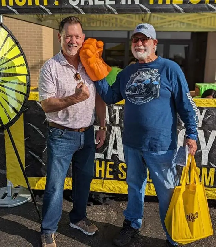 Attorney Dean Boyd posing with an attendee wearing a large orange foam fist at a community event booth.