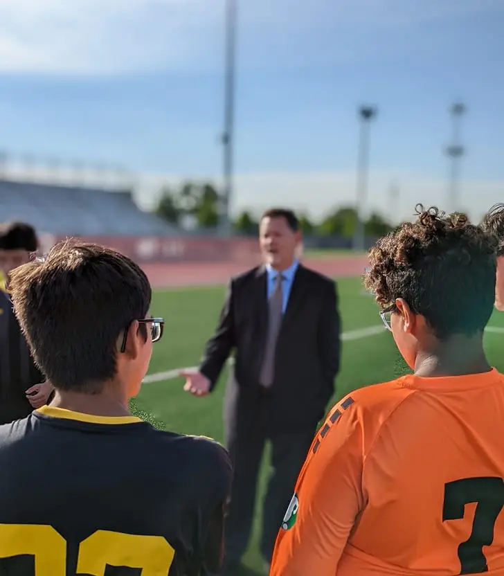 Attorney Dean Boyd speaking with young soccer players on a sports field.
